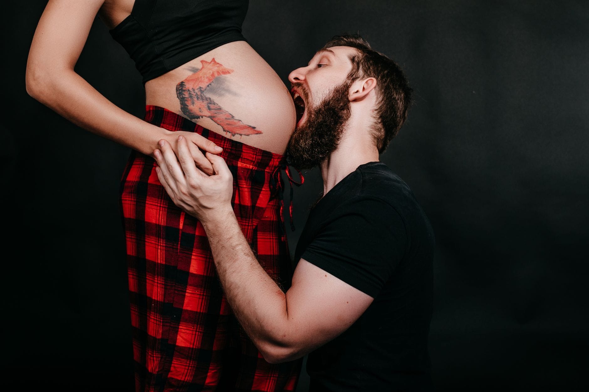 Partner całuje w brzuch ciężarną partnerkę w przytuleniu na ciemnym tle
